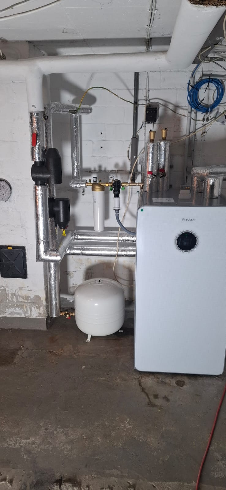 Innenaufgestellte Bosch-Wärmepumpe mit Speicher, Ausdehnungsgefäß und vollständig isolierter Rohrinstallation.